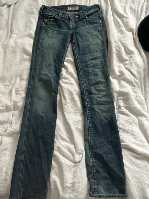Blå jeans från 1921 Jeans, bootcut - Säljer ett par blå jeans från 1921 Jeans med bootcut passform. Jeansen har klassisk femficksdesign, kontrastsömmar i rött och slitningar för en cool vintagekänsla. Materialet är mjukt jeans-tyg i bomull och benen är raka med lätt utsvängd nederdel.