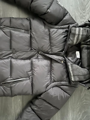Svart pufferjacka från Burberry S - Säljer en svart pufferjacka från Burberry London England i storlek S. Jackan har dragkedja, knappar och två sidofickor med dragkedja. Tillverkad i polyester och har en klassisk, stilren look med quiltad design.