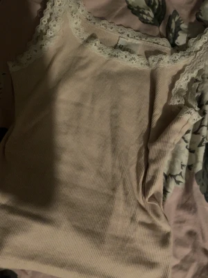 Rosa ribbad linnetopp med spets - Supersöt rosa ribbad linnetopp från H&M Divided med spetskant runt urringningen och axelbanden. Perfekt att styla med jeans eller kjol för en chill look. Tunn och mjuk i materialet, sitter snyggt och är lätt att matcha.