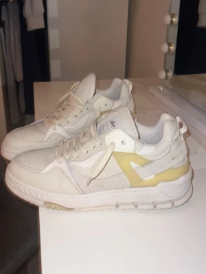 Axel Arigato vita sneakers strl 43 - Säljer ett par stilrena vita sneakers från Axel Arigato i storlek 43. Skorna har detaljer i beige och ljusgul, perforerad tå och tjock sula. Tillverkade i skinn med snörning och coola kontrastpaneler.  Pris går att diskutera 