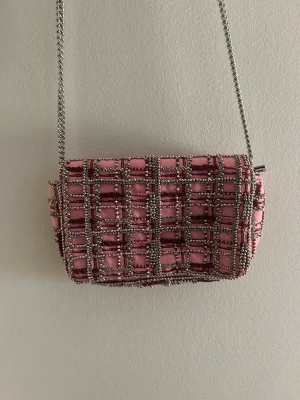 Rutig rosa axelväska från Zara - Supersnygg rosa axelväska från Zara med rutigt mönster och silverfärgade kedjedetaljer. Väskan har dragkedja och magnetlås, samt en axelrem i matchande tyg och kedja. Perfekt storlek för det viktigaste och ger en trendig touch till din outfit.
