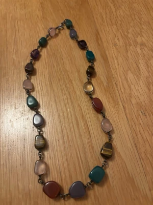 ”Antikt” kristallhalsband   -  ”Antikt” kristallhalsband. Halsbandet har 21 styck äkta kristaller. Okänd metall (märkning: R35). Halsbandet har kristaller såsom rosenkvarts och tigeröga m.fl. Halsbandet är 45 cm långt. 