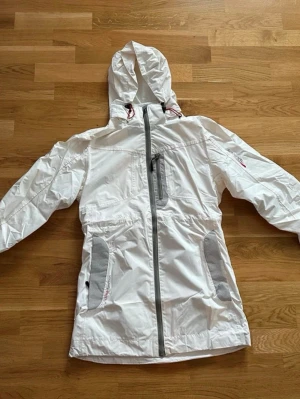 Regn/vindjacka från Autograph  - Säljer en vit vindjacka från Autograph. Jackan har hel dragkedja framtill, praktiska fickor med dragkedja och meshpaneler på sidorna. Perfekt för blåsiga dagar och outdoor-aktiviteter. Snygg och funktionell design.