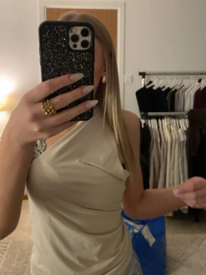 Beige oneshoulder topp med spets - Säljer en beige oneshoulder topp med snygg omlott-design och spetsdetalj vid axeln. Toppen är ärmlös och har en cool asymmetrisk form som gör den unik. Perfekt för dig som vill sticka ut med en trendig och stilren look. Jätte fin och typ helt ny passar till allt❤️