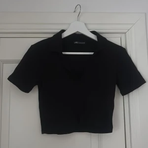 Svart croppad topp - Säljer en svart croppad topp från Zara med korta ärmar och klassisk krage. Toppen har en stilren och enkel design som är lätt att matcha med olika outfits. Perfekt för dig som gillar minimalistisk stil och vill ha något som känns både trendigt och bekvämt.