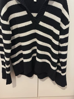 Svartvit randig stickad tröja - Säljer en svart och vit stickad tröja med breda ränder och v-ringad hals. Tröjan har lång ärm och är gjord i ett grovstickat material som känns både mjukt och rejält. Perfekt för dig som gillar en chill och stilren look.