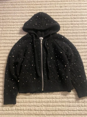 Svart stickad hoodie med pärlor från Zara - Säljer en svart kofta från Zara med dragkedja och huva. Tröjan är stickad och har pärlor över hela ytan. Använd fåtal gånger. 