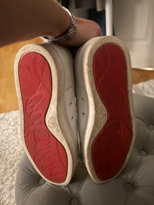 Vita Louboutin skor - Säljer ett par vita sneakers från Christian Louboutin med ikoniska röda sulor och coola nitar på tån. Skorna är i skinn och har snörning. Perfekta för dig som vill sticka ut med en lyxig och edgy vibe.
