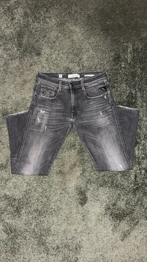 Replay grå jeans med slitningar - Snygga grå jeans från Replay med tidlösa slitningar och tvättad look. Klassisk femficksmodell och tydliga kontrastsömmar. Jeansen har en slim fit passform och är tillverkade i mjukt denimtyg för en bekväm känsla. Har du frågor är det bara att skicka! Priset är inte hugget i sten – kom med ett rimligt bud.