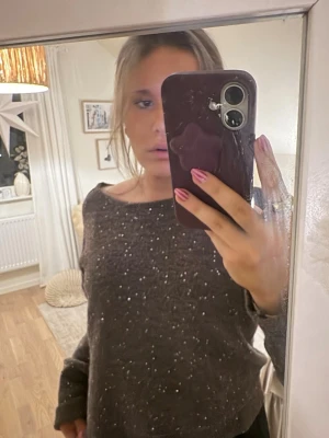 Mörkbrun stickad tröja med glitter - Mysig mörkbrun stickad tröja med glittriga paljettdetaljer över hela plagget. Tröjan har rund halsringning och långa ärmar, perfekt för att liva upp din outfit med lite extra shine. Helt ny aldrig använt.