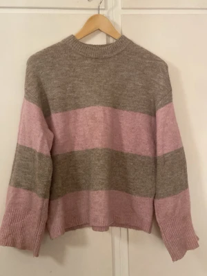 Randig stickad tröja från H&M XS - Mysig stickad tröja från H&M i storlek XS. Tröjan har breda ränder i beige och ljusrosa, rund halsringning och långa ärmar med ribbade muddar. Perfekt för dig som gillar en chill och avslappnad stil.