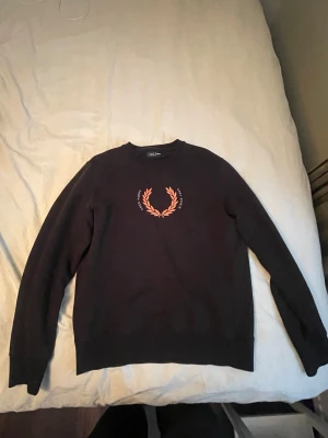 Svart sweatshirt från Fred Perry - Säljer en svart sweatshirt från Fred Perry med klassisk lagerkrans-logga på bröstet. Tröjan har rund hals och långa ärmar, perfekt för dig som gillar stilren design med en sportig touch. Materialet är mjukt och bekvämt bomull. Knappt använd!