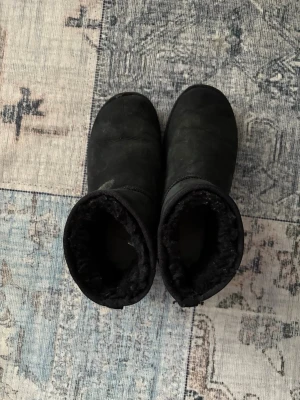 Svarta UGG boots i mocka - Säljer ett par klassiska svarta UGG boots med mjukt foder och platt sula. Skorna är tillverkade i mocka och har rund tå. Perfekta för kalla dagar och har UGG-logga baktill. Grymt sköna och värmande! Lite smutiga annars perfekta går och tvätta bort innan frakten