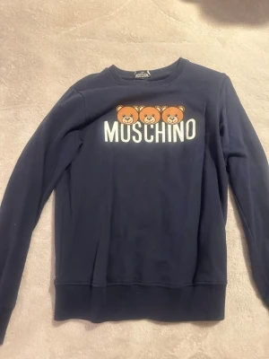 Mörkblå Moschino sweatshirt med björnar - Supersnygg mörkblå sweatshirt från Moschino med tre gulliga björnar och stor logga framtill. Tröjan har rund hals, långa ärmar och är gjord i mjuk bomull. Perfekt för dig som vill ha något trendigt och bekvämt i garderoben. Äkta tröja!!!