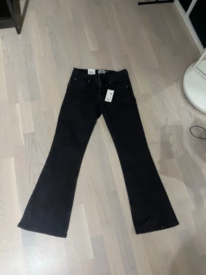 Svarta bootcut jeans från 157 - Svarta jeans från 157 med bootcut-snitt och låg midja. Klassisk femficksmodell med dragkedja och knapp framtill. Jeansen är gjorda i ett mjukt denim-material som ger en skön känsla och snygg passform. Perfekta för dig som gillar en retro vibe.