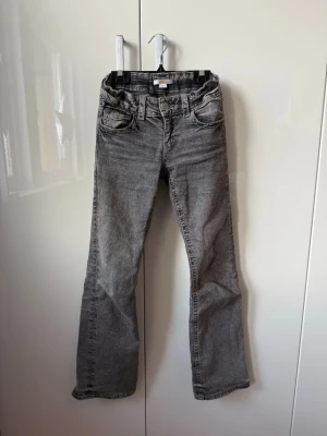 Grå bootcut jeans med broderade fickor - Snygga grå jeans ifrån Gina tricot med bootcut passform och coola broderade detaljer på bakfickorn. Jeansen är low wais med justerbar midja och är i storlek 152. Dom är använda men är i jätte fint skick💗