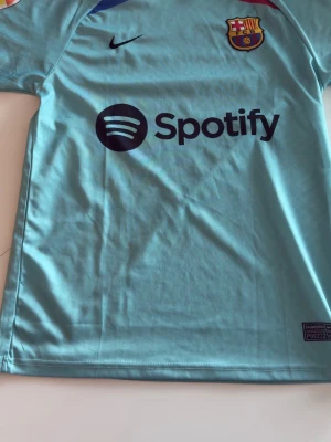 Barca Gavi tröja Nike M - Snygg Barcelona matchtröja i ljusblått med Gavi och nummer 6 på ryggen. Tröjan har Nike-logga, FCB-emblem, Spotify-tryck på bröstet och UNHCR-tryck i gult på ryggen. Tillverkad i polyester med Dri-Fit ADV-teknologi för extra komfort.har haft på mig den 2 gånger