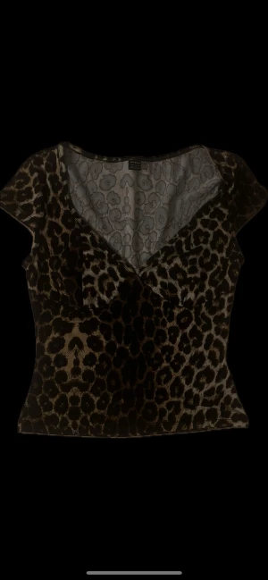 Leopardmönstrad topp från SHEIN - Leopardmönstrad topp – dam  Stilfull och iögonfallande topp med ett exklusivt leopardmönster i bruna och svarta toner. Den har en smickrande V-ringning, korta ärmar och figurnära passform som framhäver silhuetten på ett elegant sätt. Perfekt både till vardags, kvällsoutfits och festligare tillfällen.  Skick: Ny/knappt använd. Detaljer: 	•	V-ringning 	•	Figurnära och stretchig passform 	•	Mjukt, komfortabelt material 	•	Klassisk och tidlös leopardde