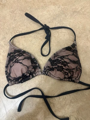 Svart spets bikini-set med knyt - Säljer ett bikini-set från Shein i storlek S med svart spetsdetalj över nude mesh. Både överdel och underdel har smala svarta band som knyts i sidorna och nacken. Snygg och trendig look med genomskinlig spets och triangelformad topp. Båda för 60kr 
