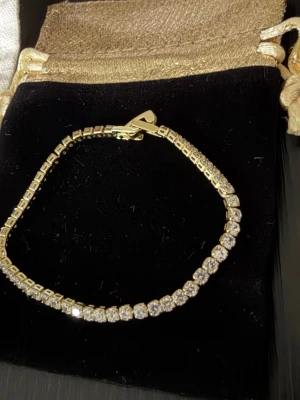 Tennis armband - Ett elegant armband med gnistrande strass stenar. Armbandet är i helt nytt skick.  OBS: kommer med presentpåse på bilden! 🎁   18k gult guld pläterad, stenar är zirconia.  Top kvalitet hållbar och super snygg och glittrig.  Går att duscha med! 2,5mm tjock 17cm lång