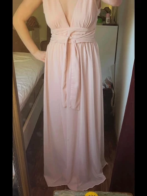 Ljusrosa långklänning med omlott - Säljer en elegant ljusrosa långklänning, (balklänning?) med omlott och djup v-ringning. Klänningen har ett brett midjeband som knyts framtill eller baktill!. Materialet är mjukt och faller snyggt längs kroppen, perfekt för sommarens speciella tillfällen