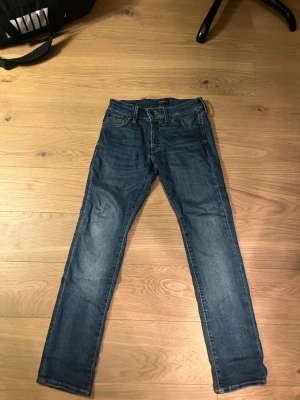 Blå jeans i storlek 27/30 - Säljer ett par klassiska blå jeans med fem fickor och raka ben. Jeansen har en snygg tvätt och är tillverkade i slitstarkt denim. Passar dig som gillar en enkel och tidlös look. Perfekt för dig som vill ha ett par jeans som funkar till allt.