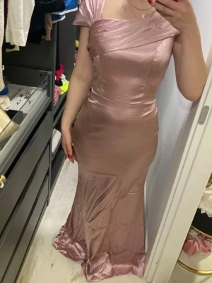 Champagnefärgad långklänning i satin - Snygg och elegant långklänning i champagnefärgad satin med figurnära passform. Klänningen har korta ärmar, omlottdetaljer vid bysten och en lätt glansig finish som ger en lyxig känsla. Perfekt för dig som vill sticka ut med en sofistikerad look.