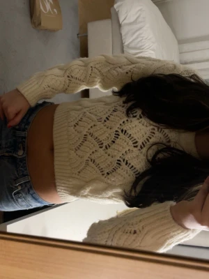 Stickad croppad tröja Rita Ora collab med Primark - Säljer en croppad stickad tröja från Rita Ora x Primark i storlek XS. Tröjan är ljusbeige med snyggt flätmönster och hålstickad design. Den har långa ärmar och bred ribbad kant vid midjan och ärmslut