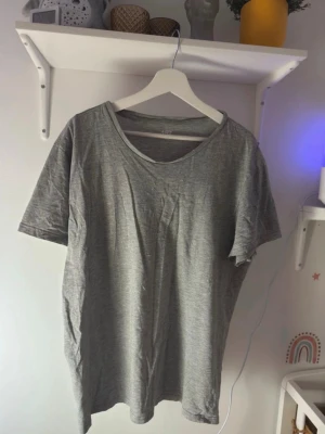 Grå basic t-shirt från 4F - En enkel och stilren grå t-shirt från 4F med rund hals och korta ärmar. T-shirten är gjord i mjuk bomull och har en loose passform som gör den skön att bära. Perfekt för dig som gillar minimalistisk stil och vill ha en klassisk t-shirt i garderoben.