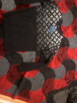 Svart tröja med vit logomönster - Säljer en svart långärmad tröja med vit logomönster över bröstet och axlarna. Tröjan har rund hals och är i ett mjukt material som känns skönt mot huden. Perfekt för dig som gillar stilrena plagg med en twist.