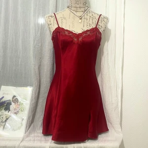 Röd satin klänning från Victoria’s Secret - Snygg röd kortklänning i satin med en liten slits framtill och en figurnära passform som ger en elegant siluett. Storlek S, passar bäst storlek 36. Sitter lite lös om du är storlek 34 och lite tight om du är storlek 38. Dockan är i storlek 36.