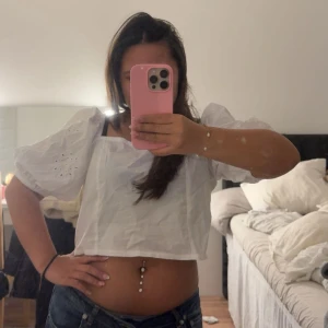 Vit croppad blus med puffärm - Säljer en vit croppad blus med puffiga, korta ärmar och broderade hålmönster. Toppen har fyrkantig halsringning och är tillverkad i bomull. Perfekt för dig som gillar romantisk och trendig stil med voluminösa detaljer.