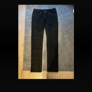 Svarta jeans från Nudie Jeans, 28/32 - Snygga svarta jeans från Nudie Jeans med klassisk femficksdesign och kontrastsömmar. Modellen har rak passform och normal midja, tillverkade i mjukt bomullsmaterial. Perfekt för dig som gillar stilrena och tidlösa jeans.