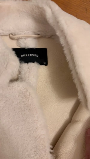 Vit pälsjacka från Reserved - Säljer en fluffig vit pälsjacka från Reserved i storlek S. Jackan har rak passform, stora fickor framtill och stängs med knappar. Perfekt för dig som vill ha en mysig och stilren look under kyliga dagar.