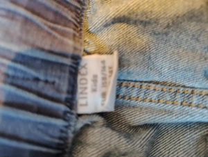 Blå jeanskjol från Lindex - Säljer en klassisk blå jeanskjol från Lindex med resår i midjan. Kjolen har fickor både fram och bak samt hällor för bälte. Perfekt för dig som gillar en enkel och tidlös denimstil.