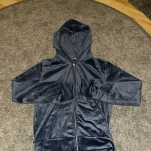 Mörkblå velour hoodie från lager 157 - Säljer en mörkblå hoodie i mjuk velour från lager 157. Tröjan har huva, hel dragkedja framtill och två fickor. Passformen är normal och materialet ger en snygg glans. Storlek S
