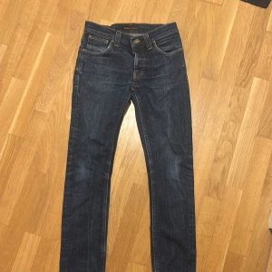 Mörkblå jeans från Nudie Jeans 30/32 - Snygga mörkblå jeans från Nudie Jeans i klassisk modell. Jeansen är slim fit Grim Tims.. Tillverkade i slitstarkt denim med subtila tvätteffekter. Perfekt för dig som gillar stilrena och tidlösa jeans.