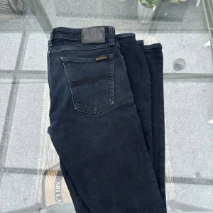 Nudie Jeans Slim Lin Black Black W31 L32 – Slim Fit - Säljer Nudie Jeans Slim Lin i färgen Black Black, storlek W31 L32. Snygga svarta jeans herr i slim fit med lätt stretch (98% bomull, 2% elastan) som gör dem bekväma och följsamma. Mörk black-black denim som är lätt att matcha och perfekt till både vardag och fest. Mycket bra skick med normalt lätt slitage men utan skador. Perfekta om du söker Nudie i slim passform eller kvalitetsjeans med bra form. 