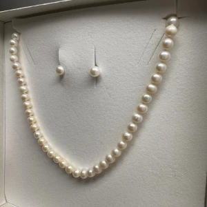 Klassiskt pärlhalsband och örhängen - Säljer ett elegant set med halsband och örhängen i äkta vita pärlor. Halsbandet består av runda pärlor i jämn storlek och örhängena är enkla pärlknoppar. Perfekt för dig som gillar tidlös och stilren design. Köpts från Albrekts guld 