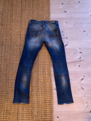 Blå jeans från Nudie Jeans - Nudie jeans i w32 asfeta jeans som har en skön fade och några astetiska hål. Kom dm vid funderingar💛