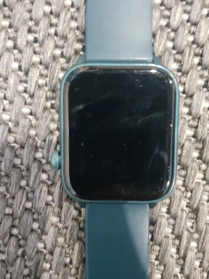 Blå smartklocka med silikonarmband - Snygg smartklocka med fyrkantig display och blått silikonarmband. Klockan har en modern look med metallfärgad ram och justerbart spänne i silver. Perfekt för dig som gillar tech och vill ha koll på tiden med stil. Kommer med laddare men utan kartong använt bara några gånger.