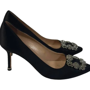 Manolo Blahnik 38 svarta pumps med strass - Svarta pumps från Manolo Blahnik i lyxig satin med spetsig tå och elegant låg klack. Dekorerade med glittrande strassdetaljer framtill som ger extra bling. Perfekt för dig som vill ha en classy och glam look. Säljes med originalkartong och dustbag.  70mm