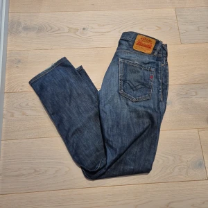 Blå Replay jeans straight fit 30/32 - Snygga blå jeans från Replay med klassisk femficksdesign och raka ben. Jeansen har en mörk tvätt med lätt slitning och detaljerad bakficka. Passar dig som gillar en enkel och tidlös stil. Midjan är normal och materialet är robust denim.