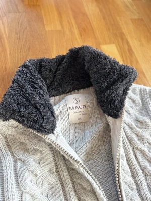 Ljusgrå stickad päls cardigan🐻 - Säljer en ljusgrå stickad kofta från MAER med mysig svart päls i kragen. Koftan har grovt kabelstickat mönster, dragkedja framtill och långa ärmar. Perfekt för kalla dagar när du vill vara både varm och snygg. Sitter som en S/M