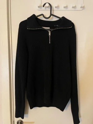 Svart stickad tröja med half zip - Svart stickad tröja från jack & jones med ribbad struktur och half zip-dragkedja vid kragen. Tröjan har långärmade och en bred krage som kan vikas ner. Perfekt för dig som gillar enkel och stilren look.