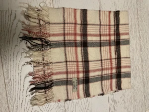 Rutig halsduk från Burberry i ull - Snygg halsduk från Burberry med klassiskt rutigt mönster i beige, svart och rosa. Gjord i mjuk ull och har fransar i ändarna. Perfekt accessoar för att lyfta din outfit och hålla dig varm under kyliga dagar.