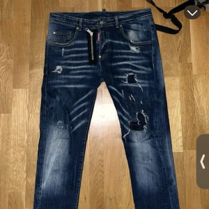 Dsquared Jens  - Säljer ett par blå jeans från Levi's med coola slitningar och hål på framsidan. Jeansen har klassisk femficksdesign, knappgylf och en mörk tvätt med ljusa detaljer. Perfekt för dig som gillar en edgy streetstil.