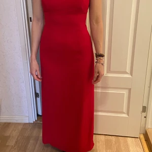 Röd långklänning med smala axelband - Säljer en elegant röd långklänning med smala axelband och figurnära passform. Klänningen har en stilren design utan mönster och en klassisk rak siluett. Perfekt för bal eller festliga tillfällen.passar 34-38
