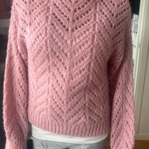 Rosa stickad tröja - Superfin rosa stickad tröja med ett snyggt hålmönster. Perfekt för kyliga dagar när du vill vara både varm och stilren. Tröjan har långa ärmar och en bekväm passform. Ett måste i garderoben för höst och vinter!