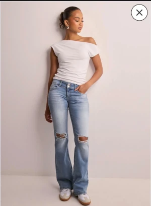 Ljusblå bootcut jeans med slitningar - Säljer ett par ljusblå bootcut jeans med snygga slitningar över knäna och klassiska fickor med lock och knapp. De är från Nelly och endast använda en gång. Säljer eftersom jag fick dom i present och kan inte lämna tillbaka. 